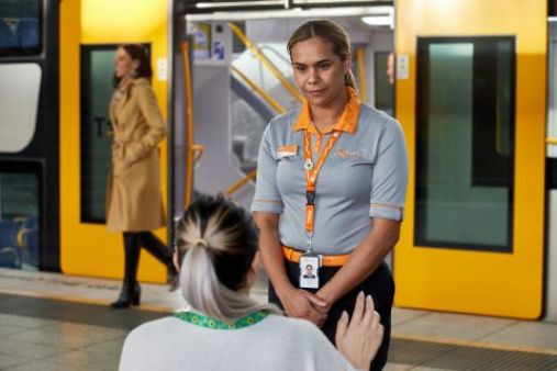 A person with a Hidden Disabilities sunflower lanyard speaking with a person in Sydney Trains uniform on a train platform