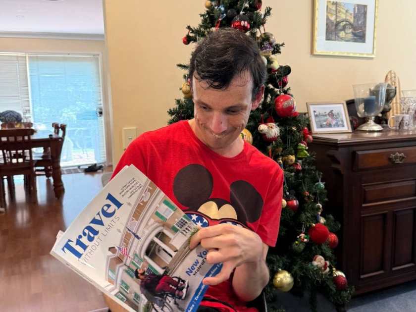 Braeden holding a copy of Travel Without Limits magazine issue 14 in front of a Christmas tree