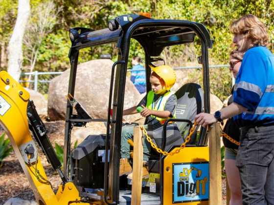 A kid operating one of the DIG IT excavators with a support person standing nearby