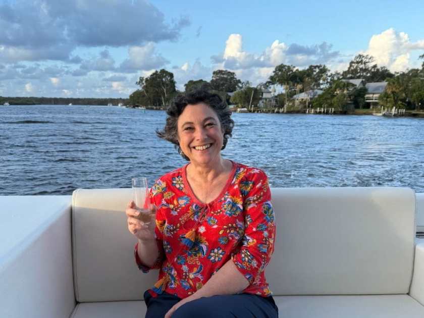 Julie holding a glass of champagne sitting on a lounge on the deck of the Noosa Stillwater
