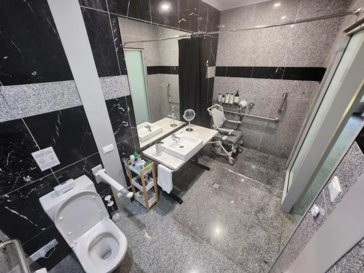 Interior view of the accessible bathroom in the UnleashedX room at Lake Macquarie Manor showing toilet, height adjustable sink and shower with chair, and grab rails throughout