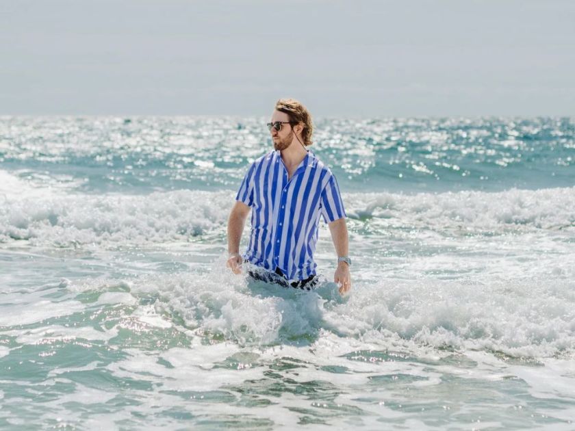 A man in the ocean wearing a blue and white striped Nashie swim shirt