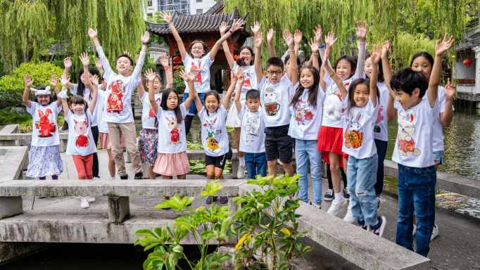 Kids celebrating the City of Sydney Lunar Festival, wearing white shirts with artwork on the front and their arms in the air